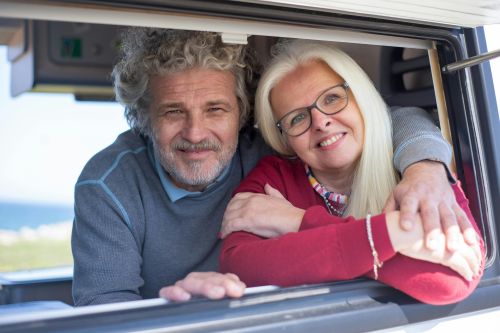 Cheerful senior couple enjoying a sunny day together, smiling and embracing in a car window.